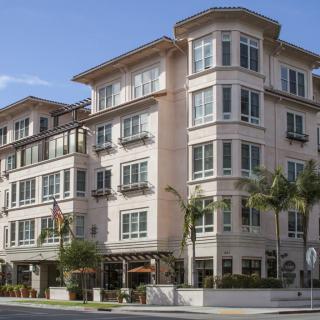 A multi-story residential building with large windows and palm trees in front, viewed from the street.