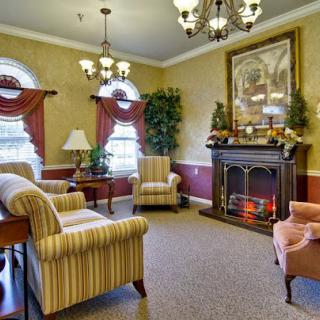 A cozy living room with a classic fireplace, armchairs, and elegant chandeliers.