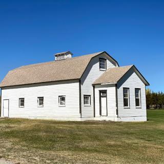 A historical rural schoolhouse set against a clear blue sky.