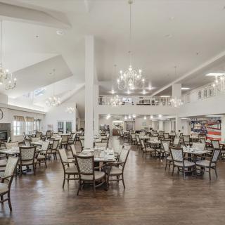 A spacious and elegantly designed dining area with multiple tables, chairs, and chandeliers.