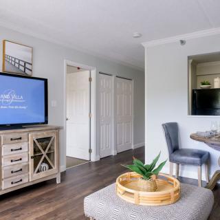 A modern living room with stylish decor, featuring a TV on a wooden stand, a cozy chair and table set, and a decorative plant centerpiece on an ottoman.