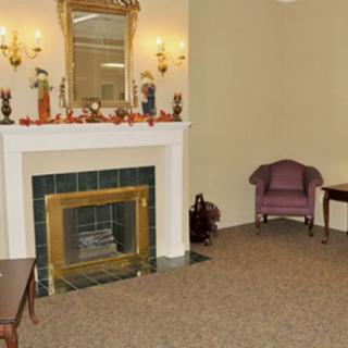 A cozy living room with a fireplace adorned with decorations, a mirror above it, and an upholstered chair in the corner.