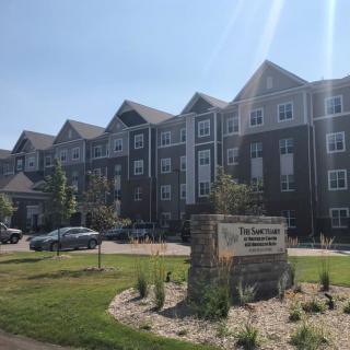 A residential apartment complex with a parking lot and a landscaped garden in front.