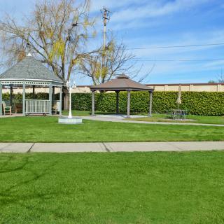 A peaceful park scene with gazebos, lush green lawn, and a clear blue sky.