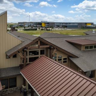 A view of a building with a metal roof and an industrial facility in the background under a partly cloudy sky.