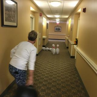 A person bowling in a hallway, aiming at pins set up at the end.