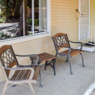 A porch with three wooden and metal chairs lined up against a yellow house wall.