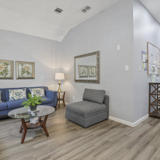 A modern living room with a blue sofa, grey seating, and wooden coffee table, complemented by wall art and a floor lamp.