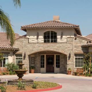 A stone facade residential building with a welcoming entrance, surrounded by palm trees and featuring a fountain in the front.