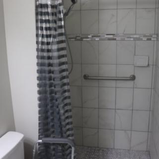 A bathroom featuring a tiled shower with a striped curtain and a grab bar.