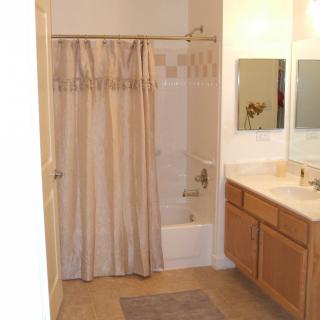 A bathroom with a shower curtain, sink, mirror, and cabinets.