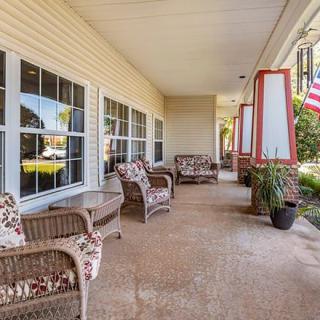 A cozy porch with wicker chairs and potted plants, featuring large windows and a view of an American flag.