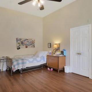 A bedroom with a bed, dresser, and lamp, featuring wooden flooring and a painting on the wall.