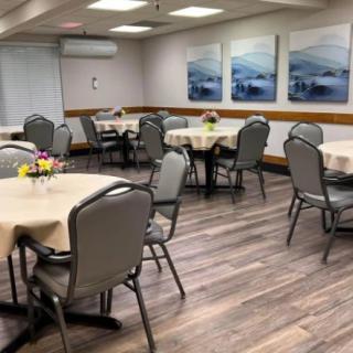 An empty dining room with neatly arranged tables and chairs, featuring decorative artwork and flower arrangements.