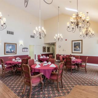 An elegant dining room with chandeliers, red tablecloths, and framed artwork on the walls.
