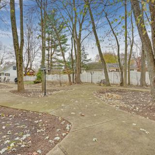 A spacious backyard with a concrete walkway surrounded by trees and a white fence.