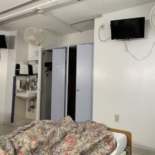 A hospital room with a bed, television, sink, and closet.