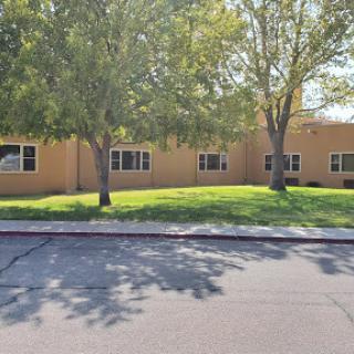 A view of a single-story building surrounded by trees and grass in a sunny environment.