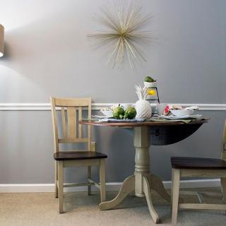A cozy dining area with a small round table, set with fruit and decor, under modern lighting and wall art.