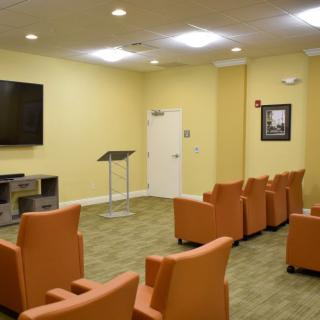 A small conference room setup with comfortable chairs, a television, and a podium.