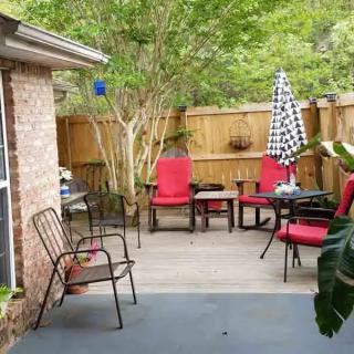 A cozy outdoor patio with red-cushioned chairs and a table under an umbrella, surrounded by greenery.