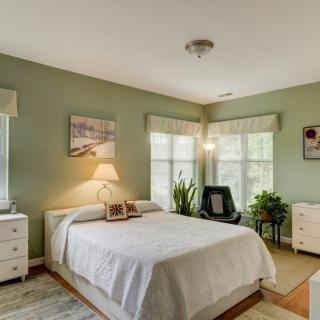 A cozy bedroom featuring a neatly made bed, large windows, and indoor plants.