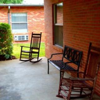 A cozy porch with rocking chairs and a bench against a brick wall.