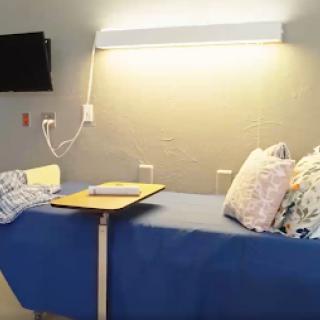 A view of a hospital bed in a patient room, equipped with pillows and a small table under soft lighting.