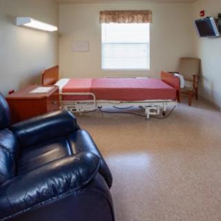 A hospital room with a bed, chair, and television.