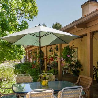 A cozy patio with a shaded umbrella, surrounded by lush greenery and outdoor seating.
