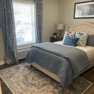 A cozy bedroom with a neatly made bed, decorative pillows, and elegant curtains.