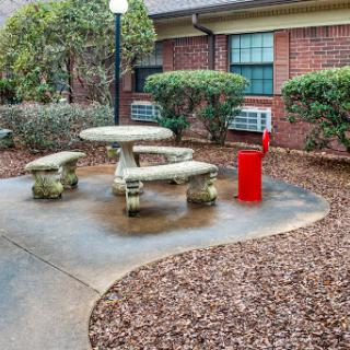 A serene outdoor seating area with a stone picnic table and benches, surrounded by landscaped plants and a striking red object.