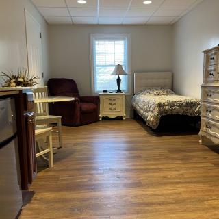 A cozy bedroom with a single bed, armchair, and a small dining table.