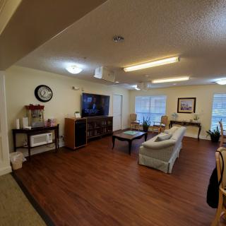 A cozy living room featuring a sofa, coffee table, and a television with wood flooring and large windows.