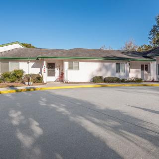 A suburban single-story building with a parking lot in front, captured on a clear sunny day.