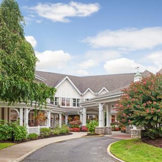 A picturesque residential building with a driveway surrounded by lush greenery and a clear sky.