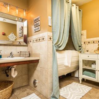 A warmly lit bathroom with a decorative tile theme, featuring a sink, mirror, and bathtub enclosed by curtains.