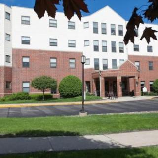 A multi-story residential building with a brick facade and an entrance canopy, surrounded by landscaped greenery.