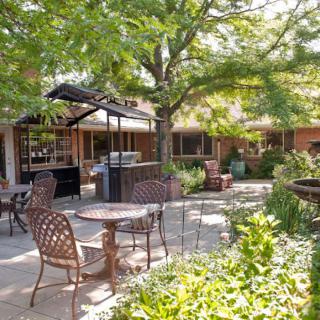 A sunny patio with tables and chairs surrounded by lush greenery.