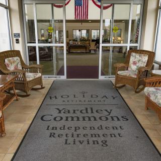 Entrance to Yardley Commons Independent Retirement Living with seating arrangements and a welcome mat.