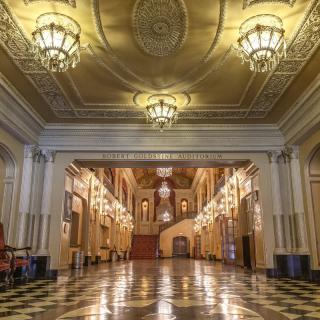 A grand and ornate interior with chandeliers and a marble floor, showcasing historic architecture.