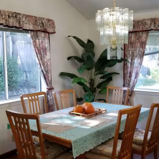 A cozy dining room with a table set for a meal, surrounded by wooden chairs and brightened by natural light filtering through the windows.