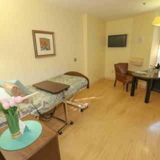 A well-furnished hospital room with a bed, table, chairs, and flowers on a side table.