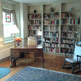 A cozy study room with bookshelves, a desk, and a rocking chair.