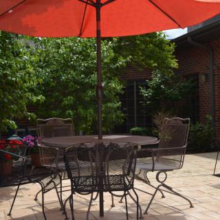 A sunny patio with a table, chairs, and a large red umbrella.