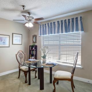A cozy dining area with a round glass table, elegant chairs, and a window draped with striped curtains.