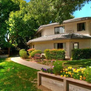 A two-story house surrounded by a lush garden with colorful flowers and tall trees on a sunny day.