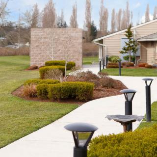 A scenic outdoor path lined with modern lighting, surrounded by well-maintained shrubs and greenery.