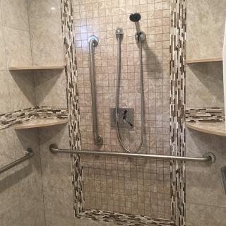 A tiled shower with multiple showerheads and built-in shelves, featuring a grab bar for safety.