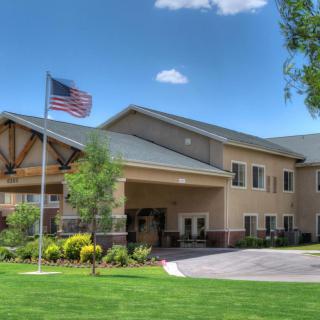A two-story building with an American flag in front, surrounded by greenery under a partly cloudy sky.